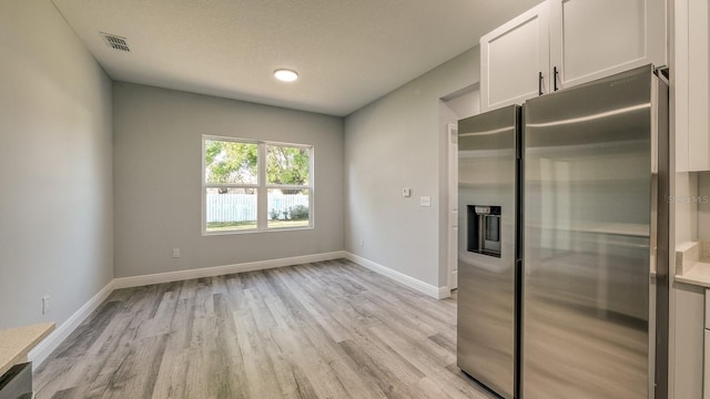 kitchen with visible vents, light wood-style flooring, white cabinets, stainless steel fridge, and baseboards