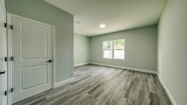 empty room featuring visible vents, a textured ceiling, baseboards, and wood finished floors