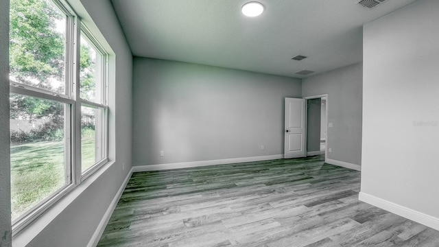 unfurnished room featuring a healthy amount of sunlight, visible vents, baseboards, and wood finished floors