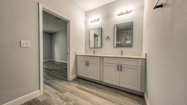 bathroom featuring wood finished floors, a sink, visible vents, baseboards, and double vanity