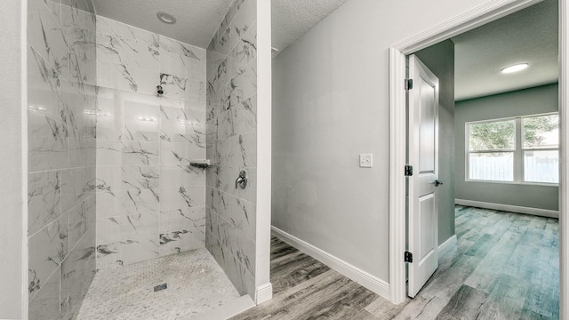 bathroom with a textured ceiling, baseboards, wood finished floors, and tiled shower