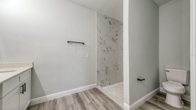 bathroom featuring toilet, baseboards, tiled shower, and wood finished floors