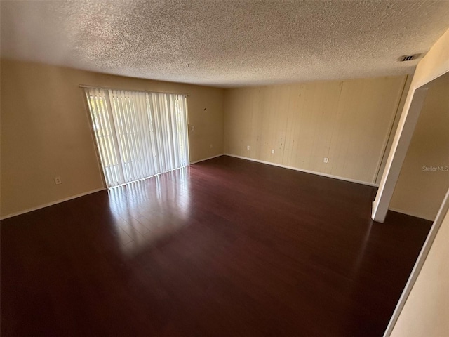 unfurnished room with a textured ceiling, dark wood finished floors, visible vents, and baseboards