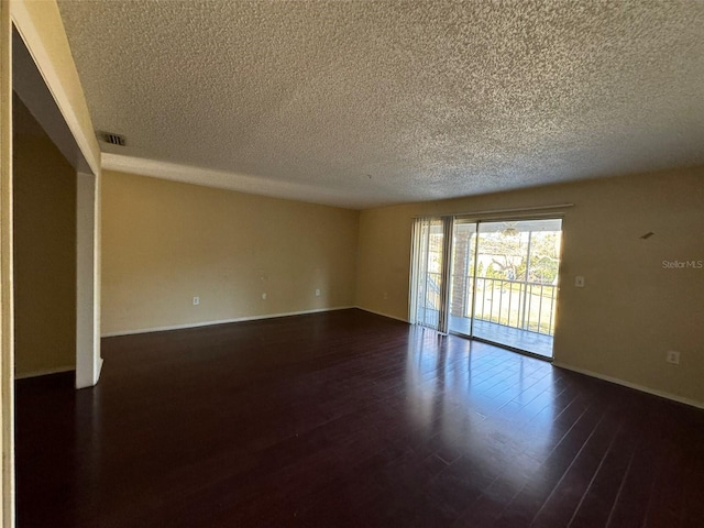 empty room featuring a textured ceiling, dark wood finished floors, visible vents, and baseboards