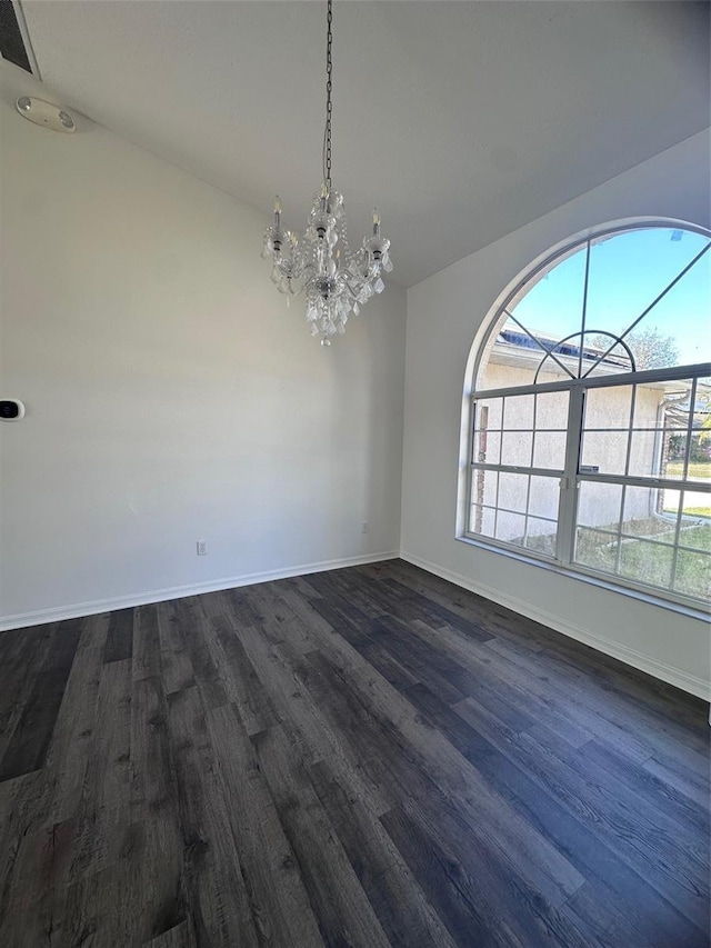 spare room with a chandelier, a healthy amount of sunlight, and dark wood finished floors