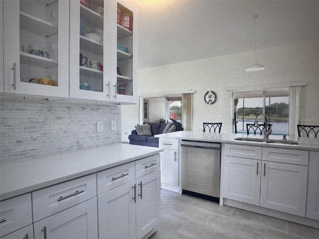 kitchen featuring light countertops, backsplash, stainless steel dishwasher, glass insert cabinets, and a sink