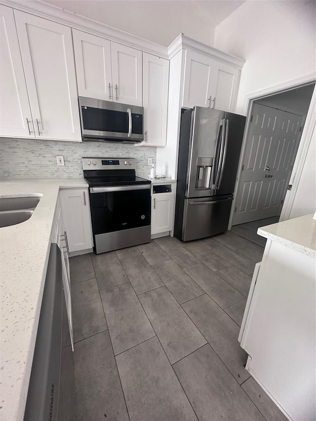 kitchen with appliances with stainless steel finishes, white cabinetry, light stone counters, and tasteful backsplash