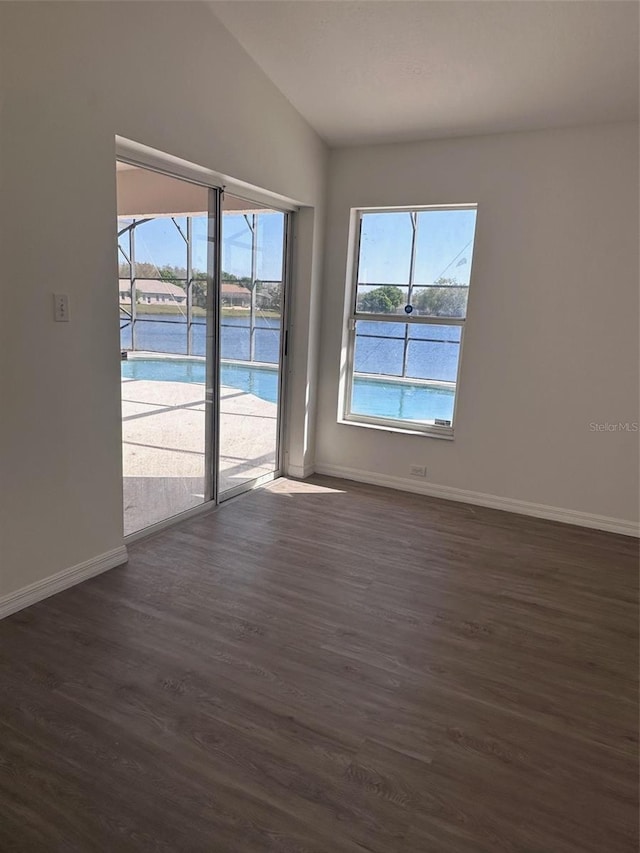 unfurnished room featuring vaulted ceiling, dark wood-style flooring, a water view, and baseboards