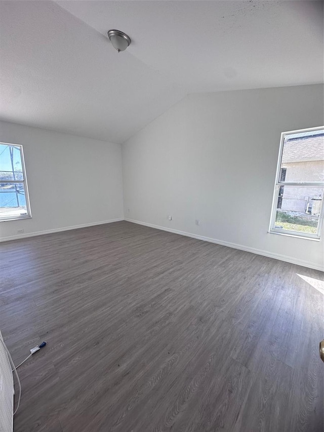 unfurnished room featuring vaulted ceiling, dark wood-style floors, and baseboards