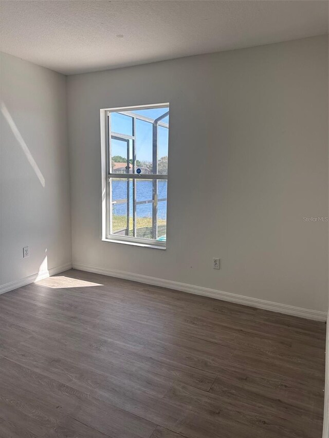 spare room with a water view, a textured ceiling, baseboards, and dark wood-type flooring