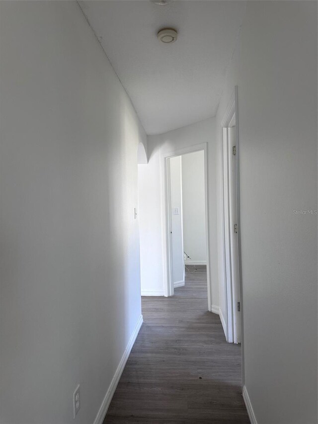 corridor featuring arched walkways, dark wood finished floors, and baseboards