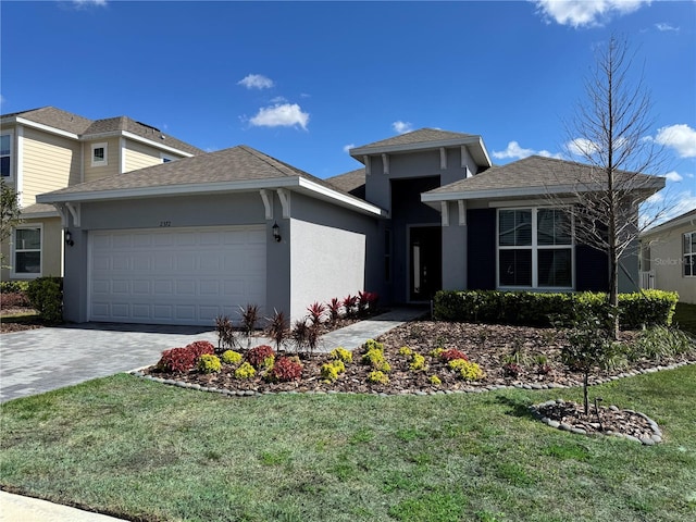 prairie-style home with an attached garage, stucco siding, decorative driveway, and a front yard