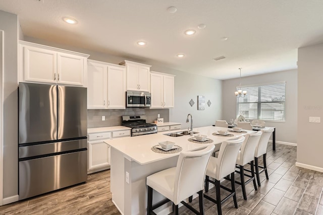 kitchen with stainless steel appliances, a sink, backsplash, wood tiled floor, and an island with sink