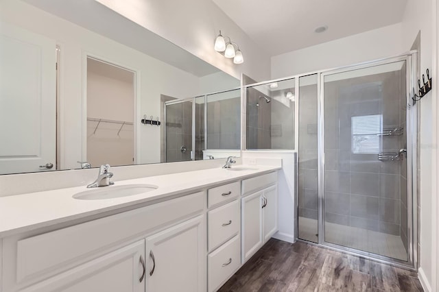 bathroom with double vanity, wood finished floors, a sink, and a shower stall