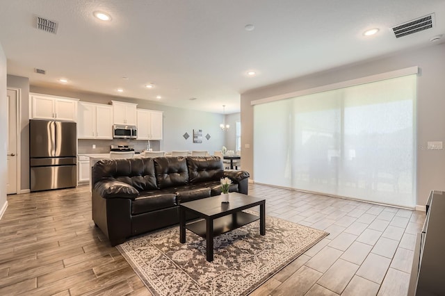 living room featuring wood tiled floor, visible vents, an inviting chandelier, and recessed lighting