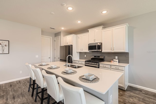 kitchen with stainless steel appliances, visible vents, decorative backsplash, a sink, and an island with sink