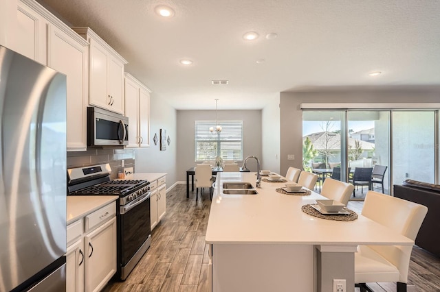 kitchen featuring backsplash, appliances with stainless steel finishes, a sink, an island with sink, and light wood-type flooring