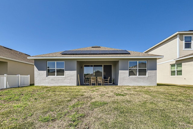 rear view of house featuring solar panels, a lawn, fence, and stucco siding