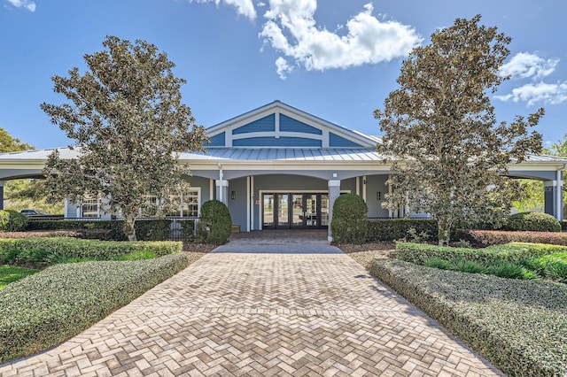 view of front of property with metal roof, a standing seam roof, decorative driveway, french doors, and a porch