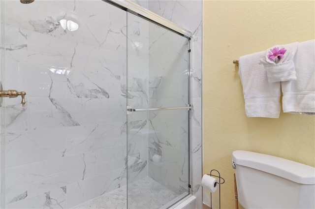 bathroom featuring a textured wall, a marble finish shower, and toilet