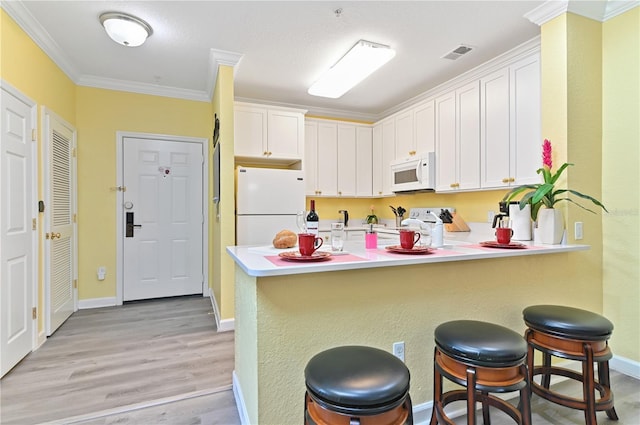 kitchen with a peninsula, white appliances, white cabinetry, and visible vents