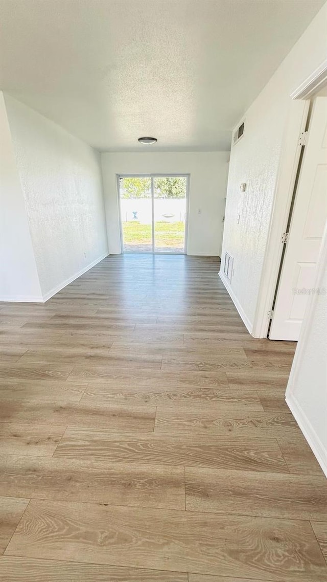 unfurnished room featuring light wood-style floors, baseboards, visible vents, and a textured ceiling