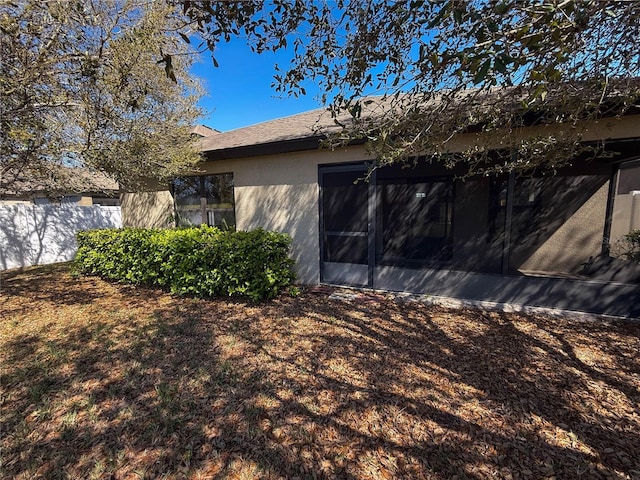 view of property exterior featuring fence, a sunroom, and stucco siding