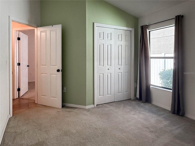 unfurnished bedroom with lofted ceiling, a closet, carpet flooring, and baseboards