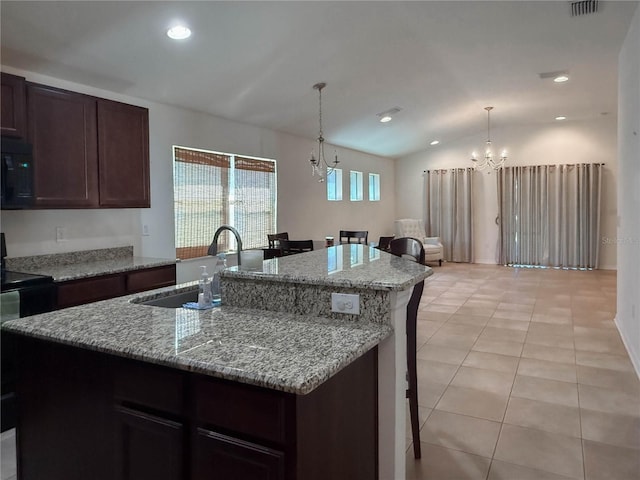 kitchen featuring a center island with sink, light tile patterned flooring, a sink, a chandelier, and black microwave