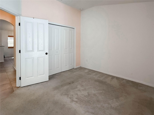 unfurnished bedroom with carpet floors, tile patterned flooring, arched walkways, and a closet