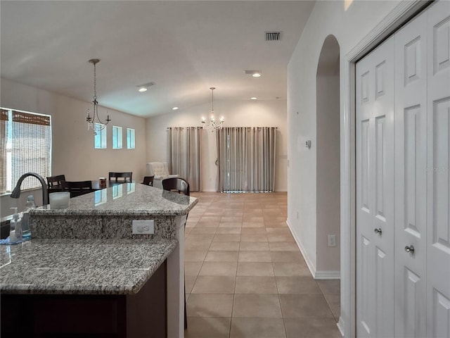 kitchen with light tile patterned floors, arched walkways, decorative light fixtures, light stone countertops, and an inviting chandelier