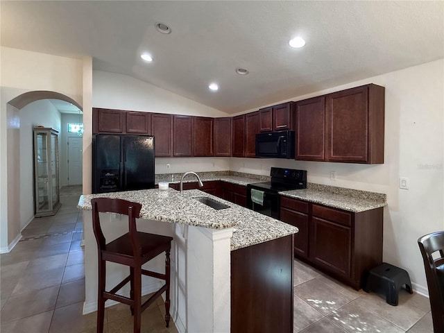 kitchen featuring arched walkways, a center island with sink, lofted ceiling, a sink, and black appliances