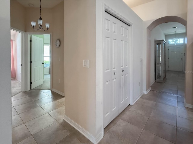 hallway with a wealth of natural light, a notable chandelier, arched walkways, and tile patterned floors