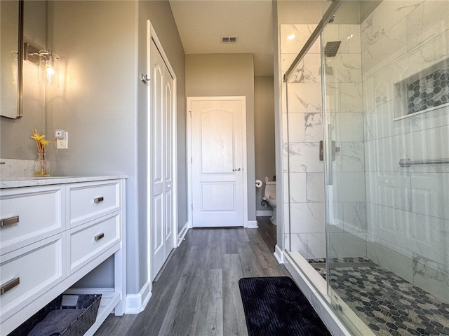 bathroom featuring toilet, wood finished floors, vanity, visible vents, and a shower stall