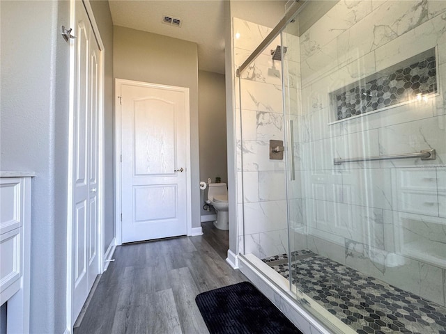 bathroom with visible vents, toilet, a shower stall, wood finished floors, and baseboards