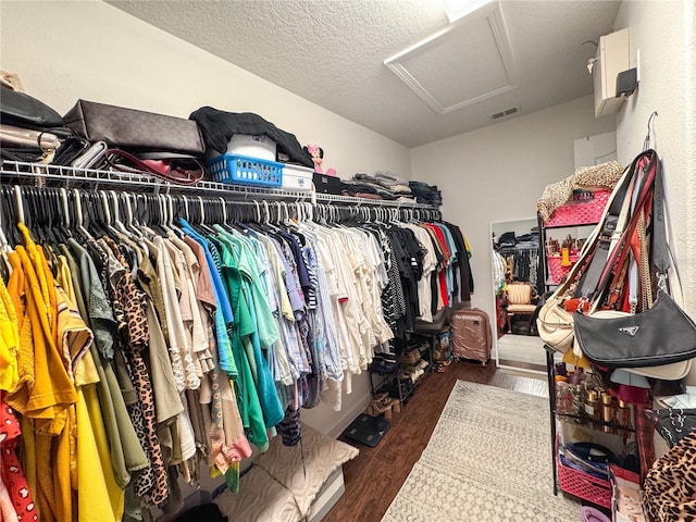 spacious closet with dark wood-style floors, visible vents, and attic access