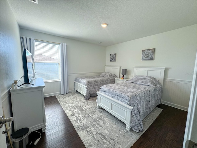 bedroom with a textured ceiling, dark wood-style flooring, and wainscoting