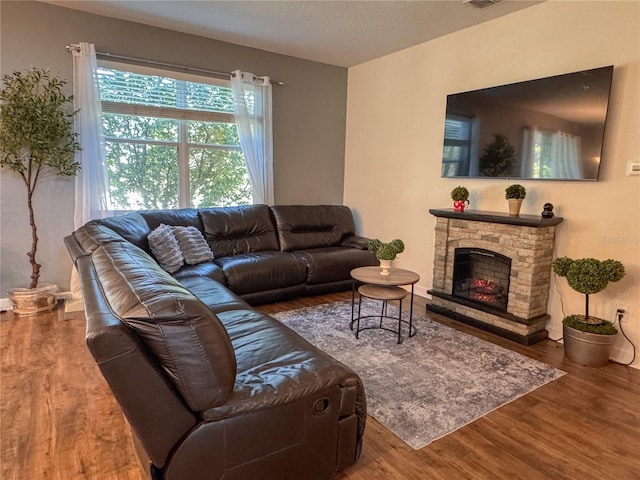 living area featuring a textured ceiling, a stone fireplace, wood finished floors, and visible vents