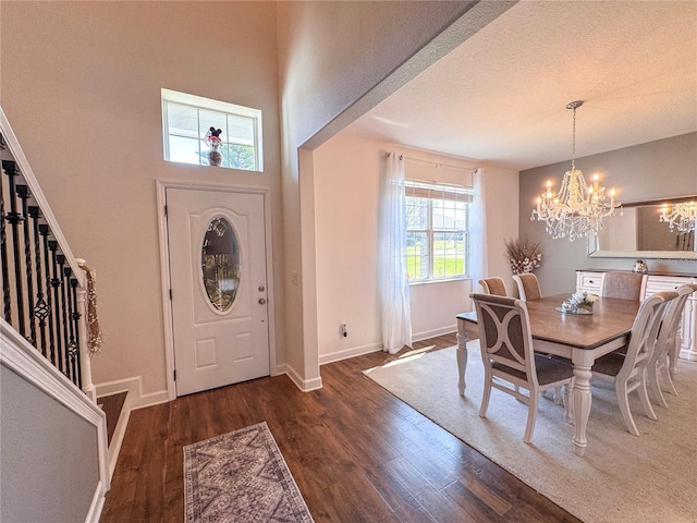 foyer entrance featuring a textured ceiling, wood finished floors, baseboards, stairs, and an inviting chandelier