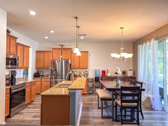 kitchen with visible vents, wood finished floors, light stone countertops, stainless steel appliances, and a sink