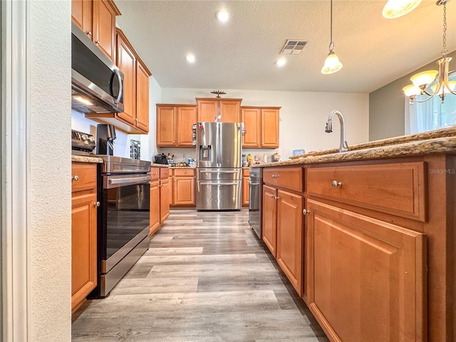 kitchen with a textured ceiling, light stone counters, visible vents, appliances with stainless steel finishes, and light wood-type flooring