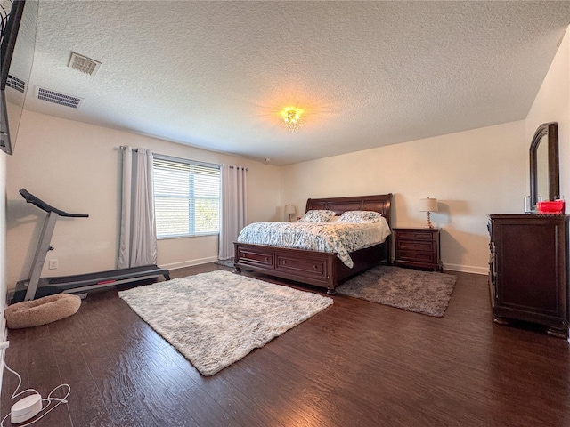 bedroom featuring baseboards, a textured ceiling, visible vents, and wood finished floors