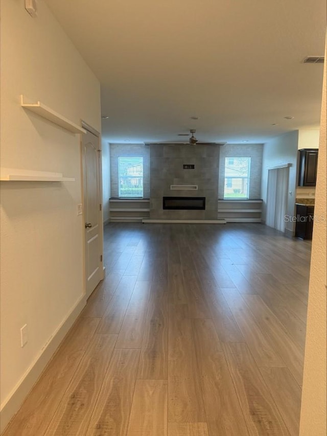 unfurnished living room with visible vents, wood finished floors, a large fireplace, baseboards, and ceiling fan