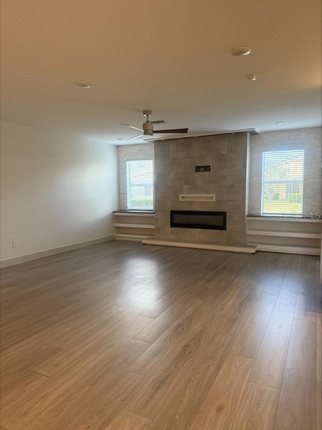 unfurnished living room featuring a wealth of natural light, a ceiling fan, wood finished floors, and a fireplace