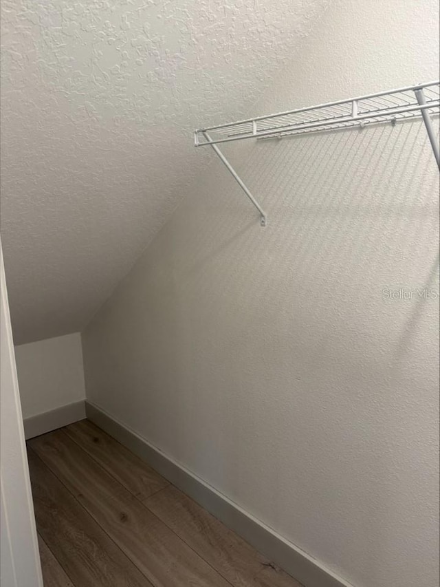 walk in closet with dark wood-type flooring and vaulted ceiling