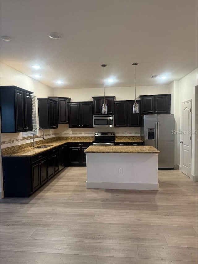 kitchen featuring a kitchen island, appliances with stainless steel finishes, dark cabinetry, light wood-style floors, and a sink