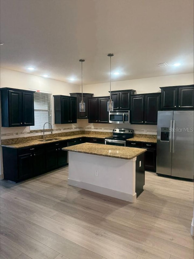 kitchen featuring a sink, a kitchen island, dark cabinetry, light wood-style floors, and appliances with stainless steel finishes