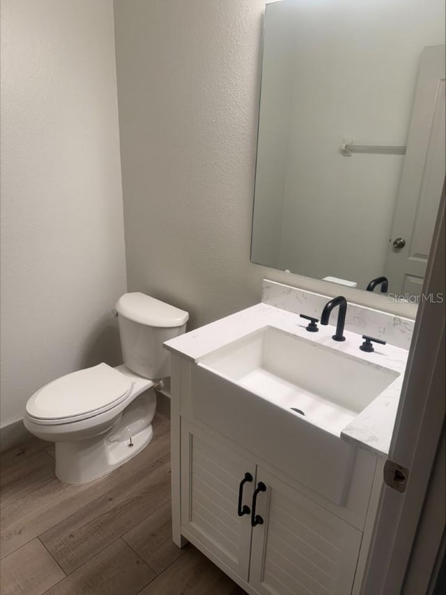 half bath with toilet, vanity, and wood finished floors