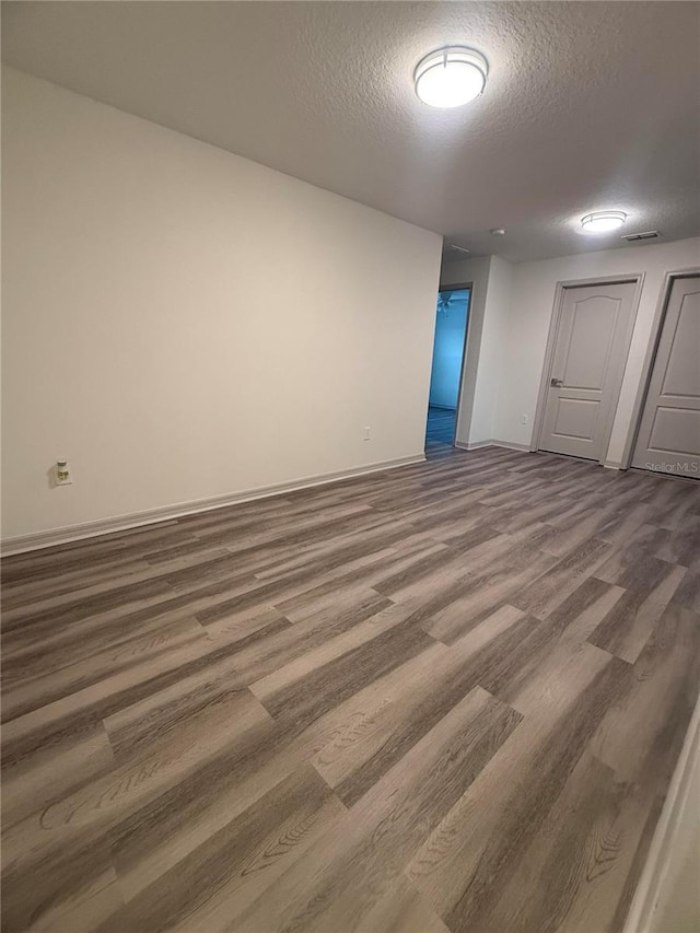 empty room featuring visible vents, baseboards, a textured ceiling, and wood finished floors