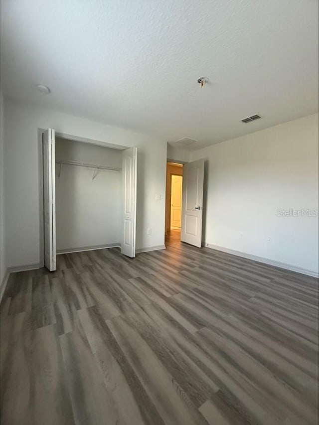 unfurnished bedroom with visible vents, baseboards, wood finished floors, a closet, and a textured ceiling